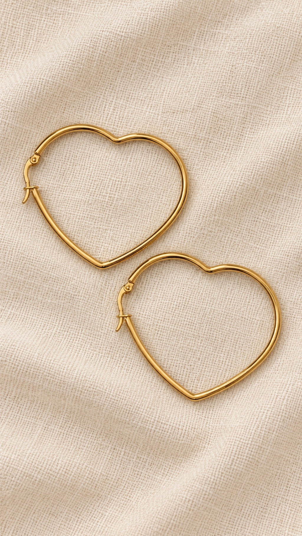 Amora Hoops – slim gold-tone heart-shaped hoop earrings on beige linen