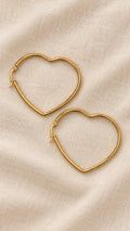 Amora Hoops – slim gold-tone heart-shaped hoop earrings on beige linen